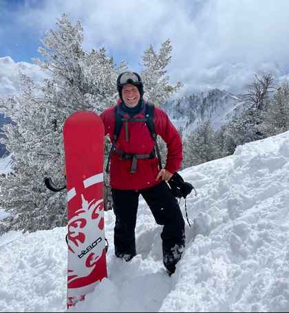 Jesse Dunlap snowboarding at Snowbasin, Utah with snow-covered peaks behind him