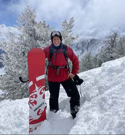 Jesse Dunlap snowboarding at Snowbasin, Utah with snow-covered peaks behind him