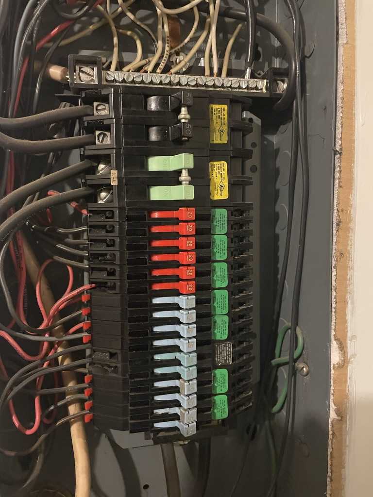 Inside of a Zinsco panel with colored breaker handles visible: blue 15-amp, red 20-amp, and green 30-amp breakers with wiring exposed